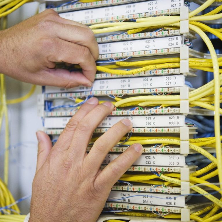 Hände, die an einem Kabelnetz mit vielen gelben und weißen Leitungen arbeiten.